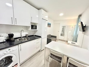A compact kitchen with white cabinets, a microwave, a coffee maker, and a washing machine. - Metro Avenida de América 09 (1-bedroom apartment) (Madrid)