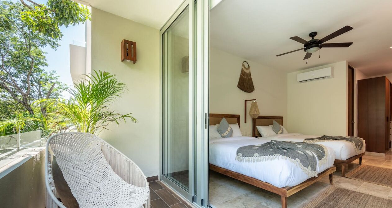 A hotel room with a bed, a ceiling fan, a window, and a balcony with a chair.