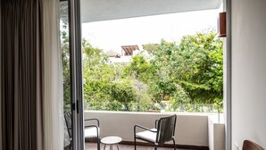 A balcony with two chairs and a small table, overlooking a lush green landscape and a building in the background. - NHOA 203A Lux 2BR Condo Pool View in Aldea Zama (Tulum)