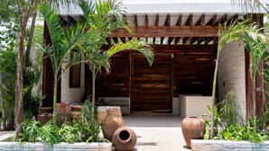 A pool area with a wooden pergola, stone walls, and tropical plants. - NHOA 203A Lux 2BR Condo Pool View in Aldea Zama (Tulum)