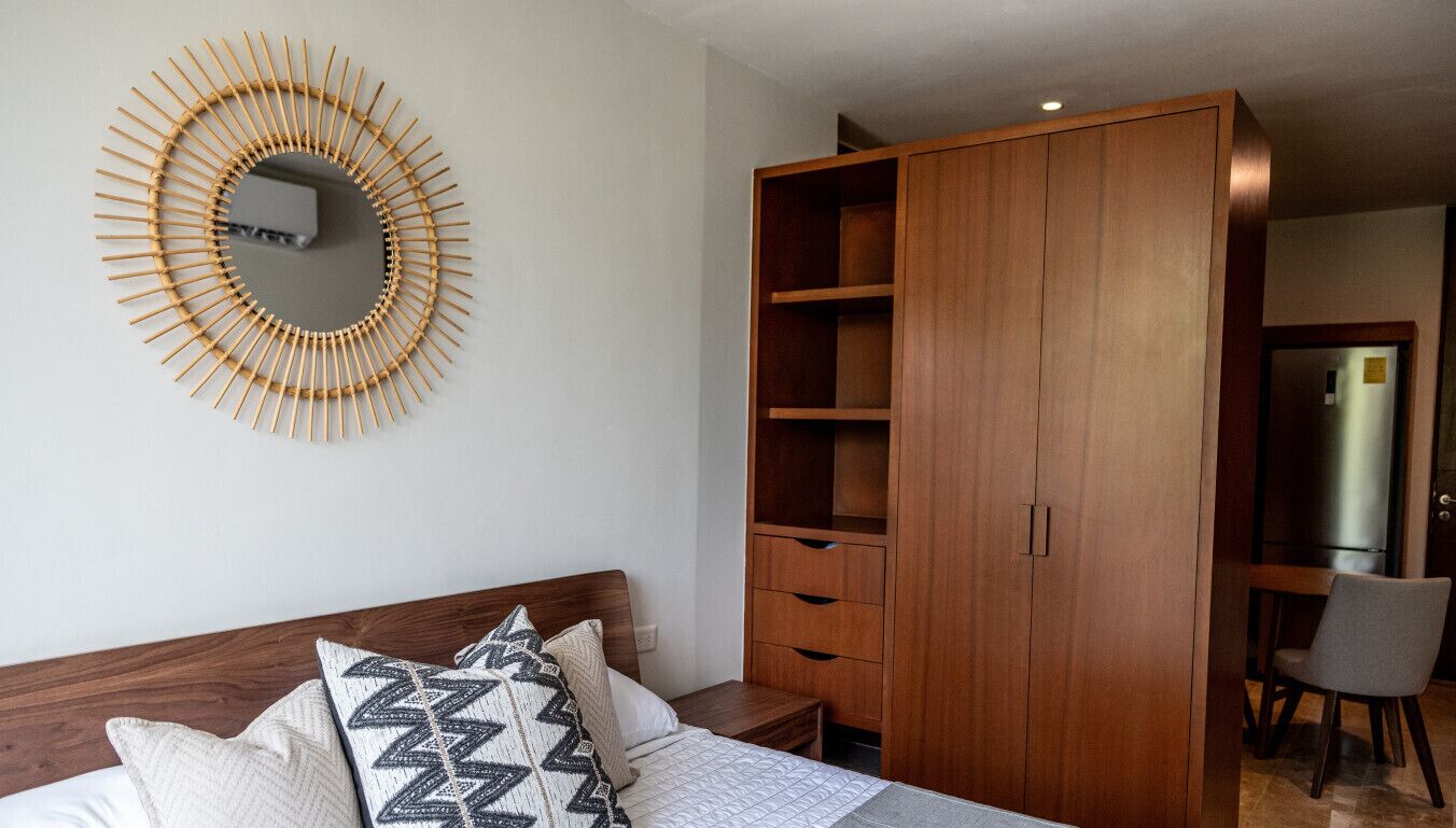 Une chambre à coucher comprenant un lit, une armoire en bois, un miroir et un bureau avec une chaise.
