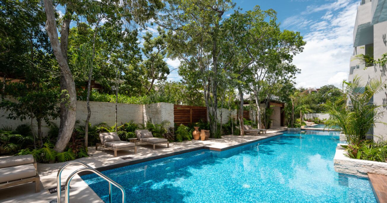 A swimming pool with lounge chairs, surrounded by trees and a brick wall.