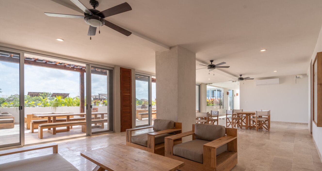 A spacious indoor area with wooden furniture, ceiling fans, and large windows offering views of the outdoors.