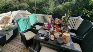 A deck with outdoor furniture, including a sofa and chairs, and a table set with food and drinks. - Room-bed & Breakfast in Stockholm (Bromma)