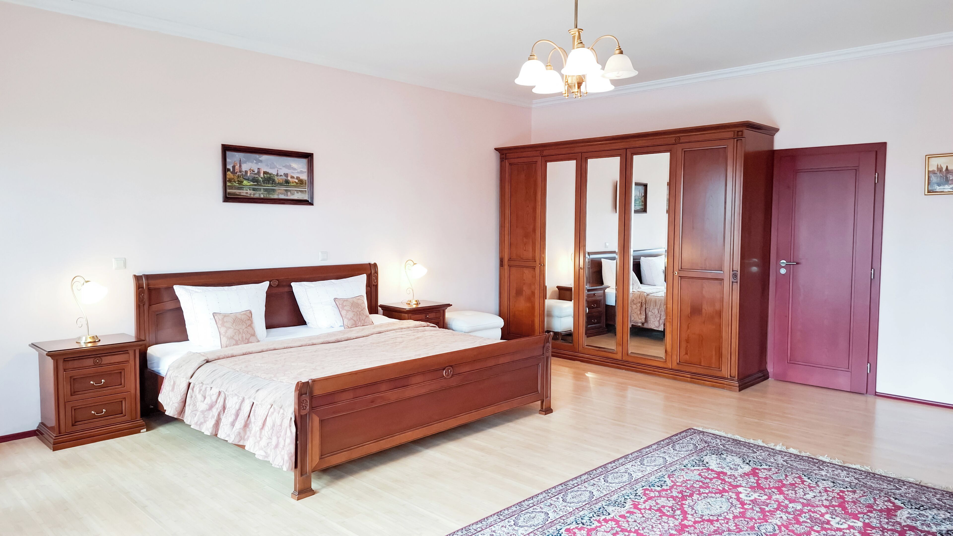 Une chambre à coucher avec un lit en bois, des tables de chevet, une armoire, un miroir et un lustre.