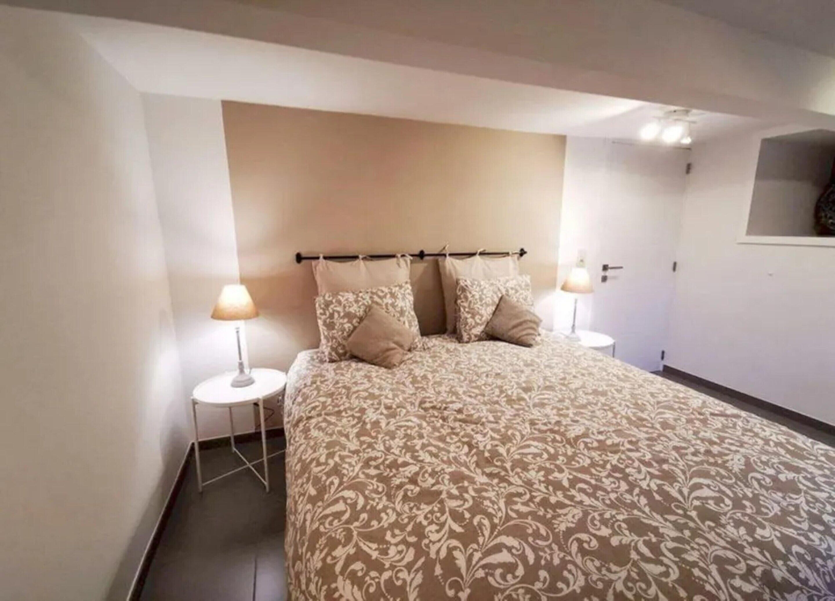 A bedroom with a large bed, two bedside tables with lamps, a headboard, and a small window.