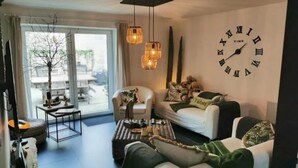 A modern living room with a large wall clock, a sofa set, a coffee table, and a view through the glass door. - Cottage in Houyet Near Lesse River Trails (Houyet)
