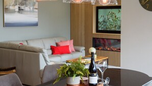 Una sala de estar moderna con un sofá, una mesa de centro con una botella de vino y una copa, y lámparas colgantes.