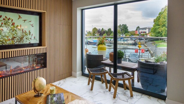 Una habitación moderna con un ventanal grande, paneles de madera, un globo terráqueo y dos sillones de mimbre.