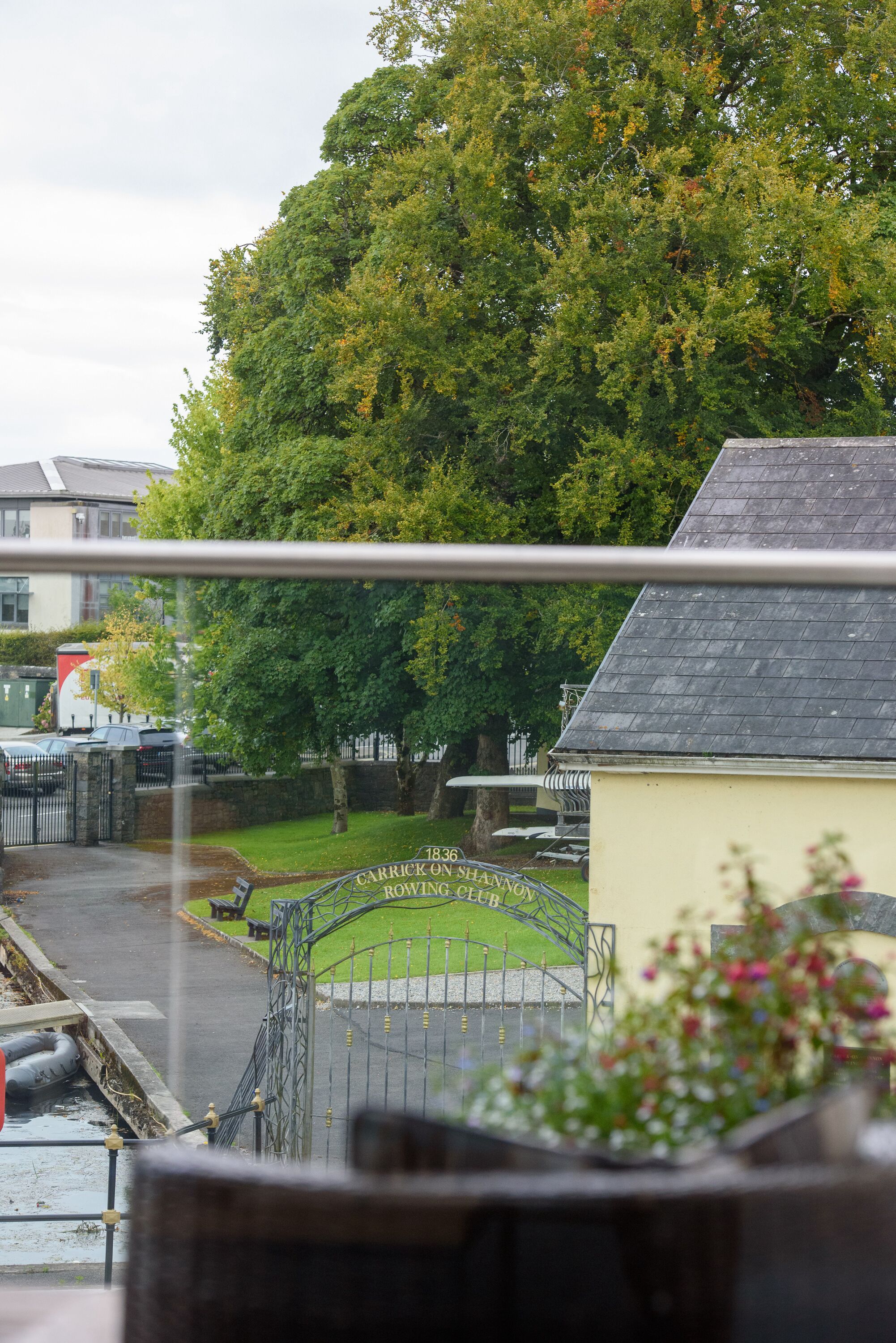 A view of a gated area with a sign reading "1836 Carrick on Shannon C.B." and a building with a grey roof.