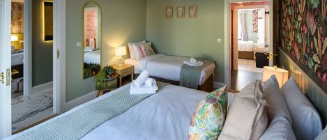 A hotel room with two beds, a mirror, a small table with a lamp, and a bathroom visible through an open door.