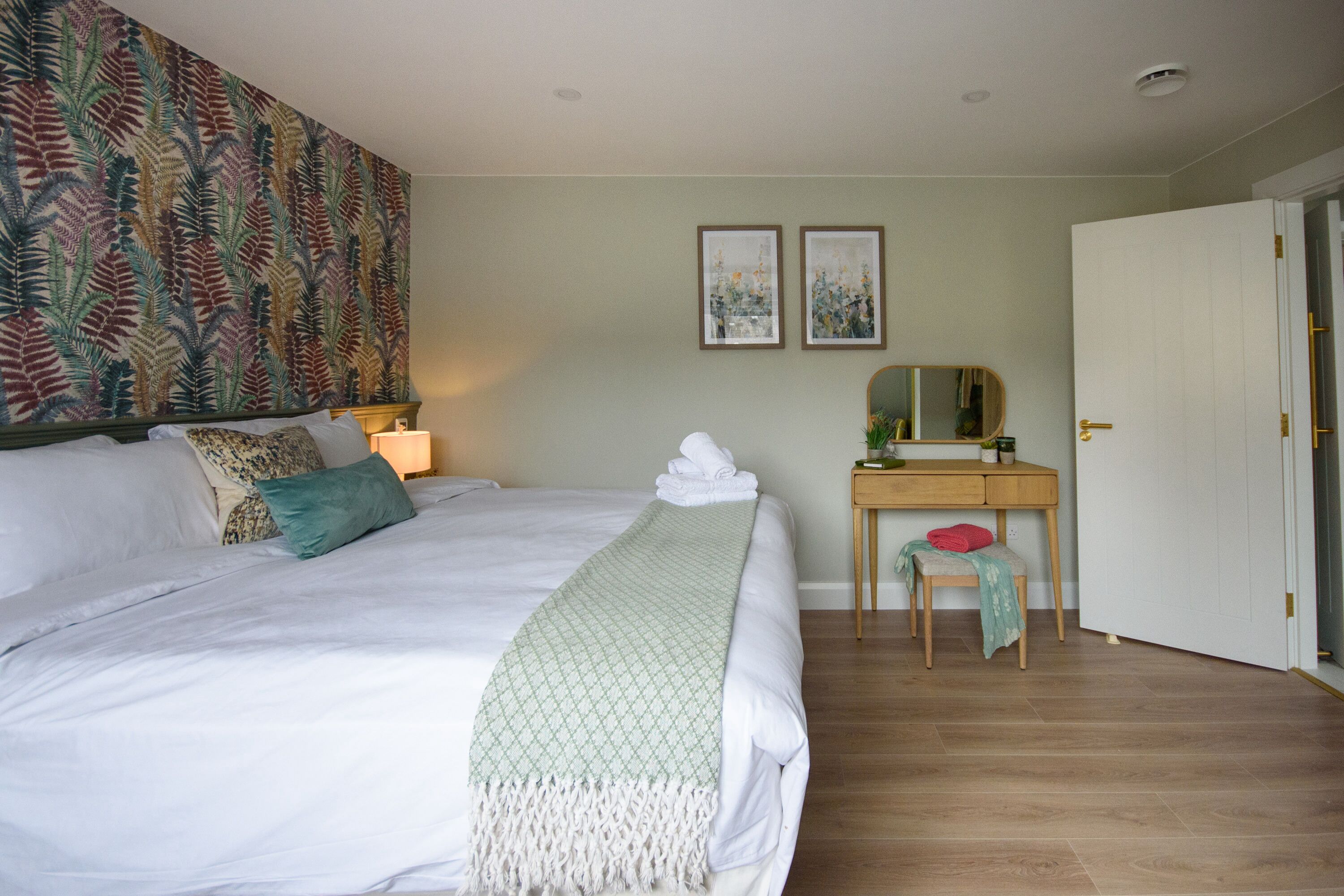 A neatly arranged bedroom with a bed, bedside table, and a desk with a chair.