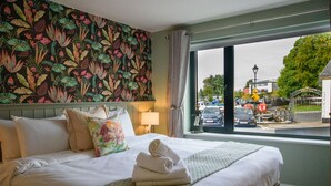 Habitación de hotel con una cama grande, un papel tapiz estampado con motivos florales y vistas a la calle.