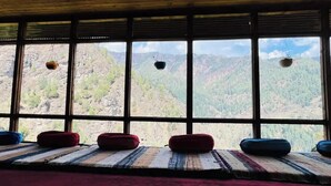 A room with large windows offering a view of a mountainous landscape. There are several cushions on the floor.