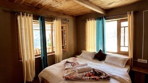 A wooden-paneled room with a large bed, curtains, and a view through the window.