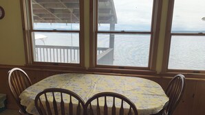 A dining area with a table and four chairs, large windows with a view of the water, and a wooden deck outside. - Charming Vintage Lakefront Cottage on Seneca Lake (Penn Yan)