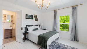 Une chambre à coucher comprenant un lit, une table de chevet, une commode, une fenêtre avec des rideaux et un lustre.