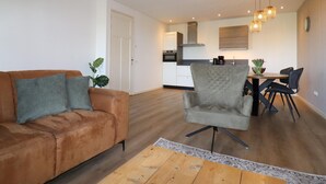 A modern living room with a brown sofa and a grey armchair, a wooden coffee table, and a dining area with a table and chairs. - Apartment in Workum Near Ijsselmeer Beach (Workum)