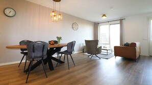 A modern living room with a wooden dining table, grey chairs, a sofa, and a large window. - Apartment in Workum Near Ijsselmeer Beach (Workum)