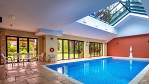 An indoor swimming pool with a skylight, stone flooring, and a view of the outdoors. - Loft in Cotswolds With Pool & Scenic Gardens (Chipping Norton)