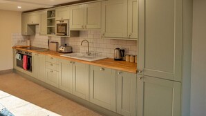 Une cuisine avec des meubles de couleur vert clair, un plan de travail en bois, un évier, une bouilloire et un grille-pain.