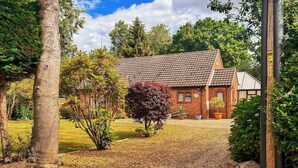 A brick house with a tiled roof, surrounded by a garden with a gravel driveway.
