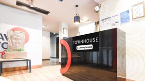 Un comptoir d’accueil portant l’inscription « TOWNHOUSE », avec un panneau indiquant qu’il est entretenu par l’entreprise, une statue de Bouddha et une plante sur une table.