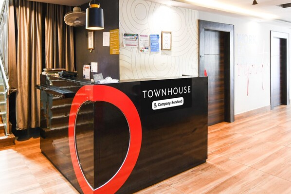 A reception desk with a 'TOWNHOUSE' sign, a company-serviced label, and a wall with circular patterns and informational posters. - Classic Chandrasekharpur (Bhubaneshwar)