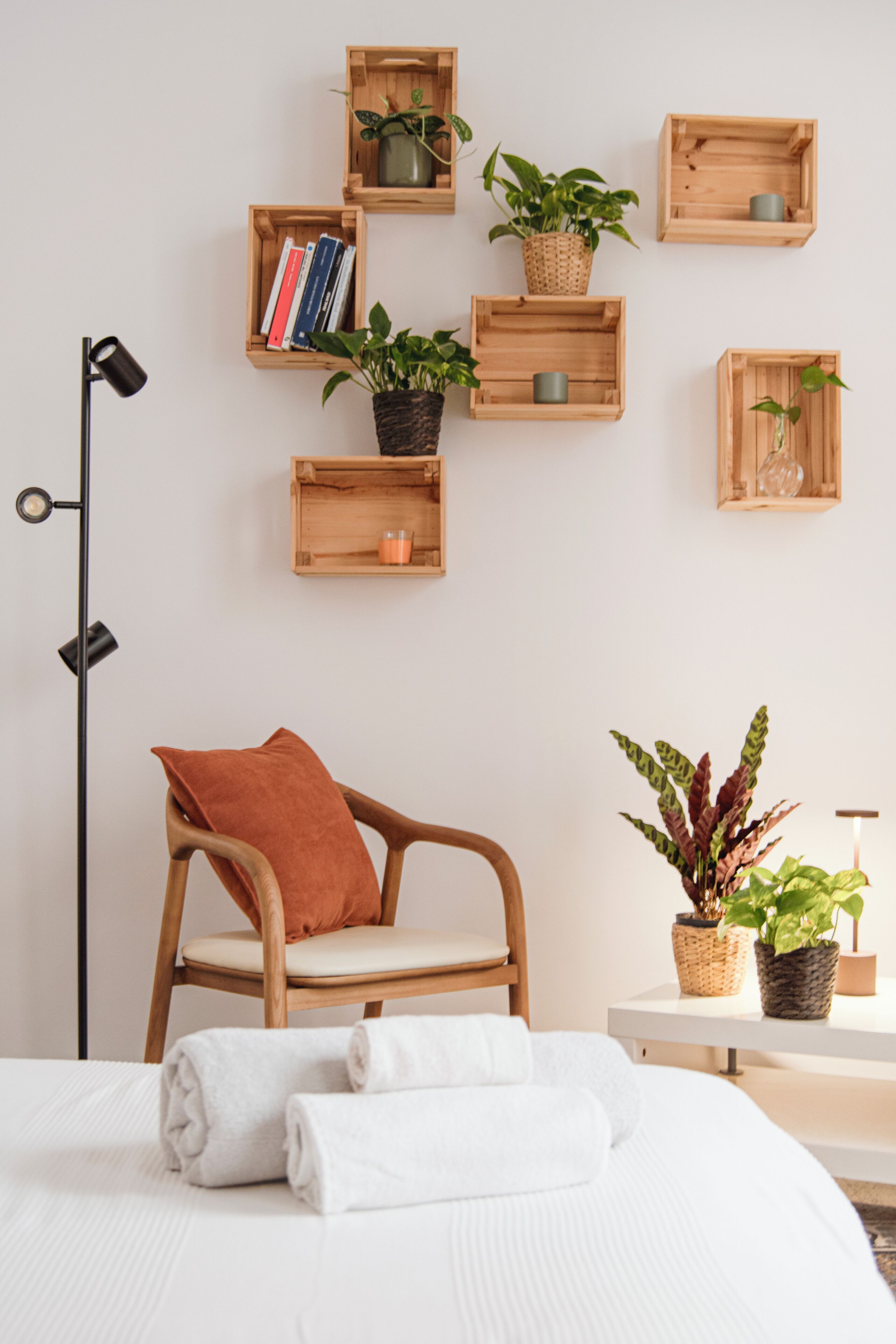 Ein ordentlich eingerichtetes Schlafzimmer mit Bett, Sessel, Nachttisch und Wandregalen mit Büchern und Pflanzen.