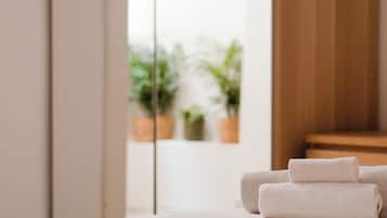 Un letto ben rifatto con una testiera in legno, un'ampia finestra vista piante in vaso e una porta scorrevole in vetro.
