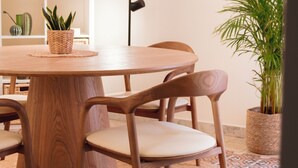 Una mesa de madera redonda con cuatro sillas, rodeada de plantas en macetas y un tapete estampado.