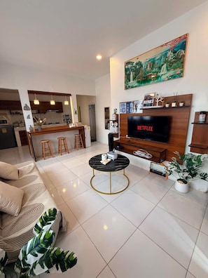 Een moderne woonkamer met een flatscreen-tv, een eethoek met barstoelen en een keuken op de achtergrond.