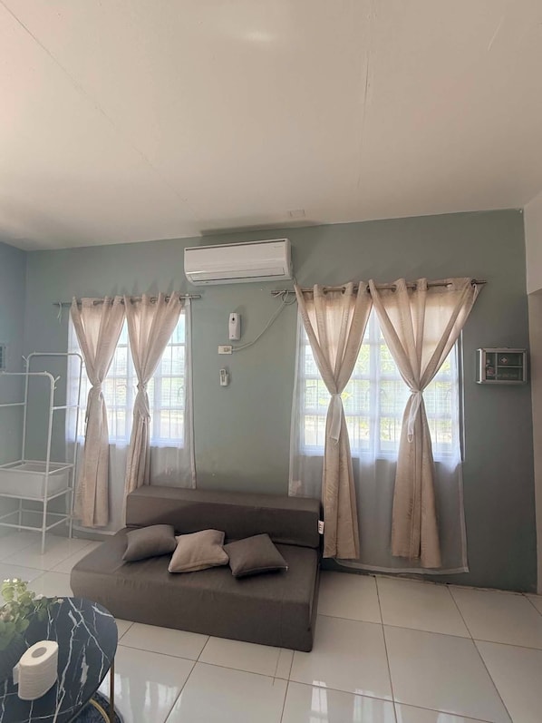 A room with a bed, curtains, an air conditioning unit, and a window.