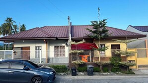 Un immeuble d’habitation avec un auvent rouge, une voiture garée et un ciel dégagé.