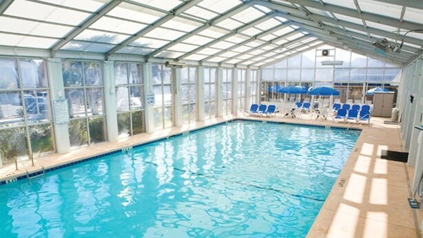 An indoor swimming pool with clear glass walls, blue lounge chairs, and umbrellas.