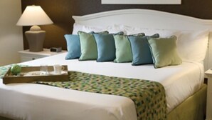 A neatly made bed with a patterned bedspread, a tray with cups and a fruit, and a lamp on a bedside table.