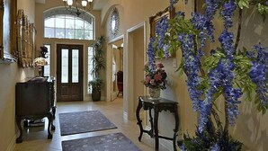 A hallway with a chandelier, a wooden bench, a potted plant, and a vase of flowers.