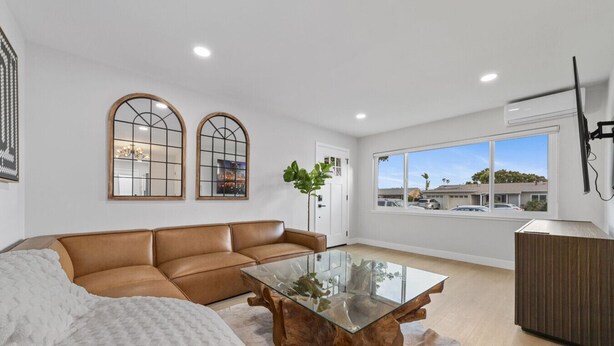 A modern living room with a leather sofa, a glass coffee table, and a large window with a view of a parking lot.