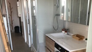 A modern bathroom with a glass shower enclosure, a built-in sink, a washing machine, and a toilet.