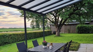 Une terrasse extérieure avec une table et des chaises, une pergola et une vue sur un champ verdoyant et des arbres.