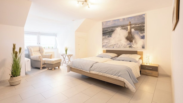 Une chambre moderne avec un grand lit, une chaise, une petite table et une plante en pot.