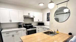 Una cucina moderna con mobili bianchi, un'isola in legno, elettrodomestici in acciaio inossidabile e uno specchio rotondo sulla parete.