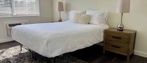 Ein Schlafzimmer mit einem Bett, Nachttischen, einem Teppich und Fenstern mit Jalousien.