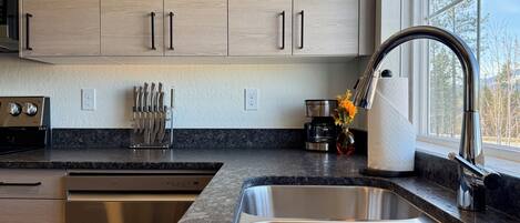 A modern kitchen with stainless steel appliances, a granite countertop, and a window with a view of trees.