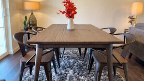 A dining area with a wooden table, six chairs, a vase with red flowers, two lamps, and a small cactus plant. - Homestead Village - Two Bedroom Condo Top Floor (Sandpoint)