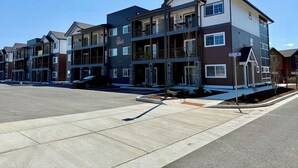 A multi-story residential building with balconies, a parking lot, and a clear sky. - Homestead Village - Two Bedroom Condo Top Floor (Sandpoint)