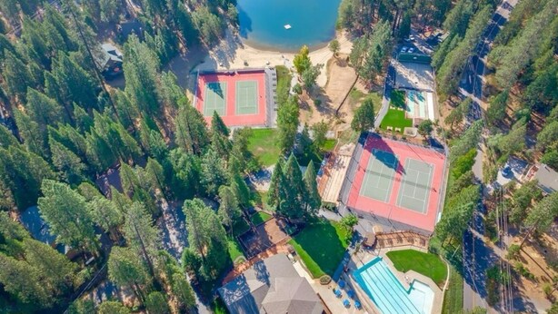 Vue aérienne d’un complexe hôtelier doté d’un court de tennis, d’une piscine et d’une plage, le tout entouré d’une forêt dense.