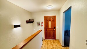 Un couloir avec un plancher en bois, une main courante en bois, une porte avec une fenêtre et un mur bleu.