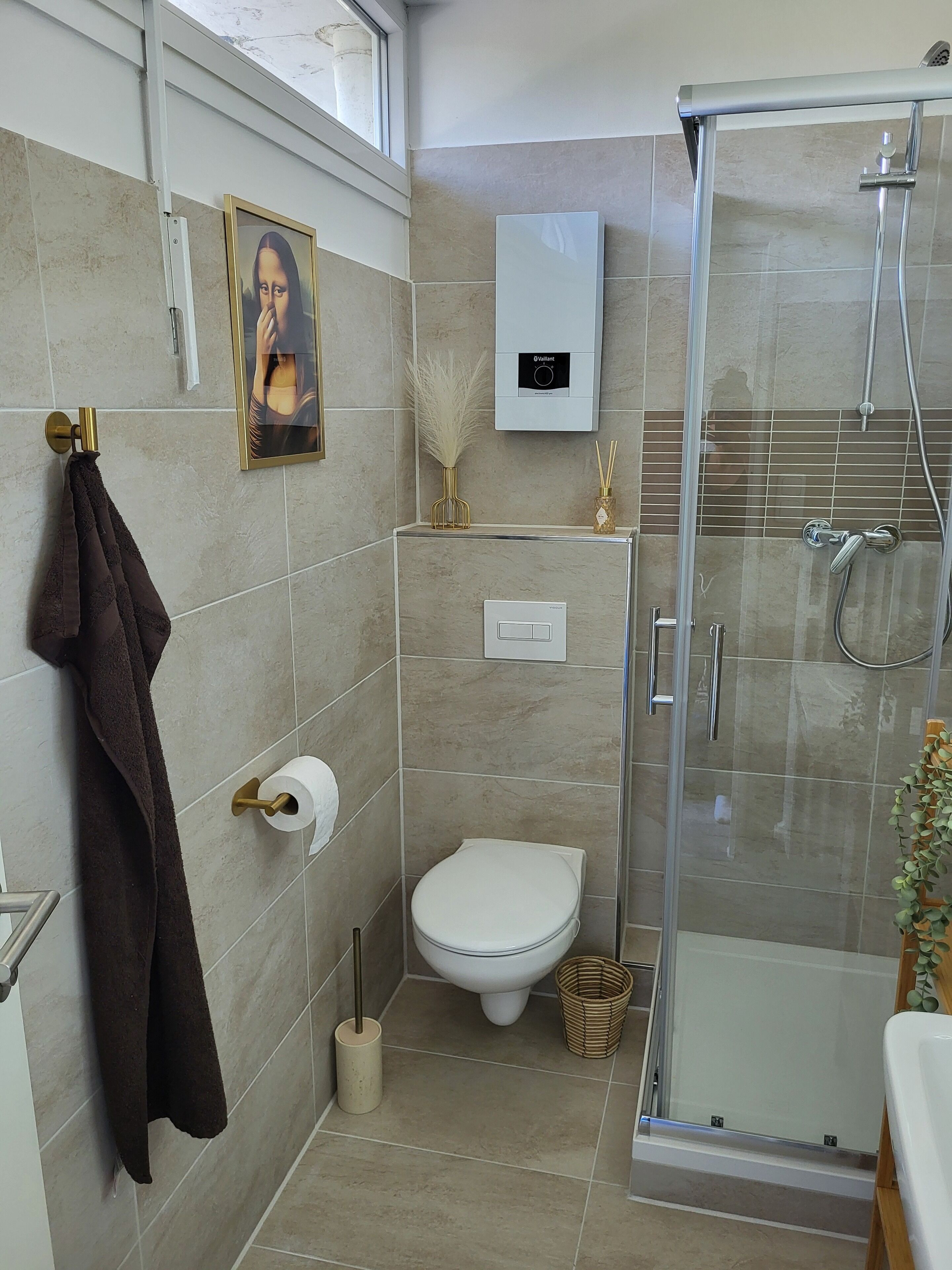 Un bagno moderno con cabina doccia in vetro, un water, un appendi asciugamani e un quadro incorniciato a parete.