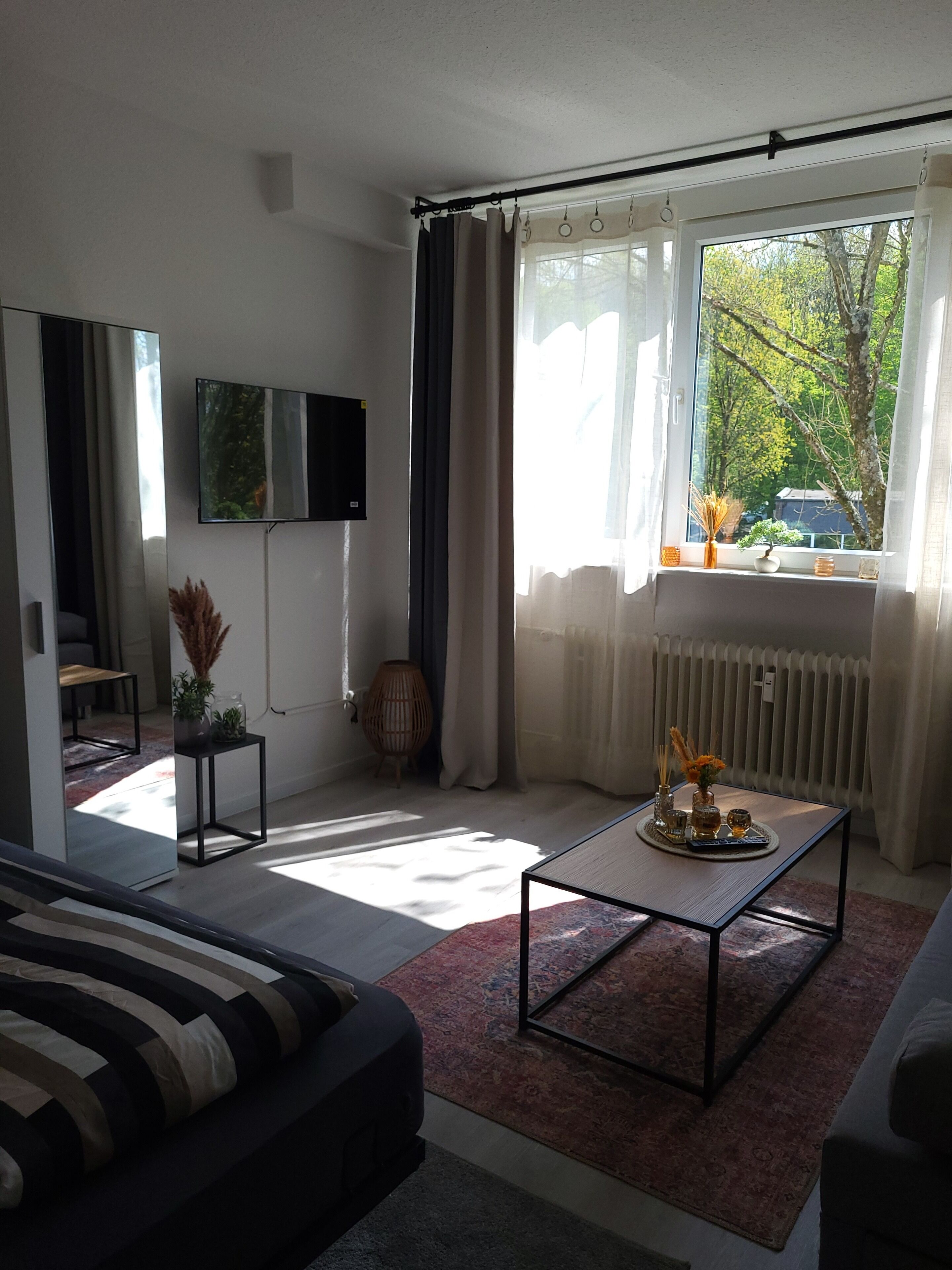 Ein modernes Wohnzimmer mit einer Couch, einem Couchtisch, einem an der Wand befestigten Fernseher und einem Fenster mit Vorhängen.